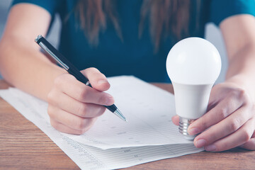 woman holding a light bulb and taking notes