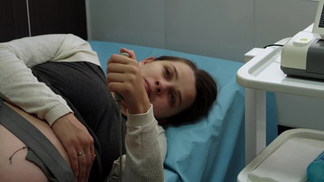 Young Pregnant Woman On Hospital Couch During Medical Control Cardiotocography. Visit Gynecologist Doctor At Clinic For Pregnancy Consultant. Examine Expectant Belly Baby Mother Healthcare Check Up