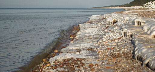 Icy stones on a sunny winter day by the Baltic sea beach, which look like little white balls,...