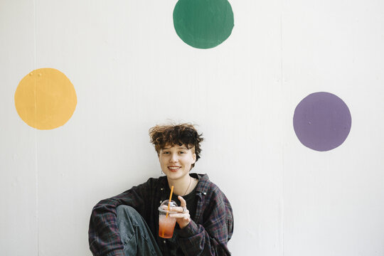 Portrait of smiling teenage boy drinking against polka dots on white wall