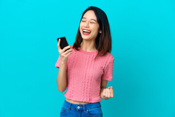 Young Vietnamese woman isolated on blue background with phone in victory position