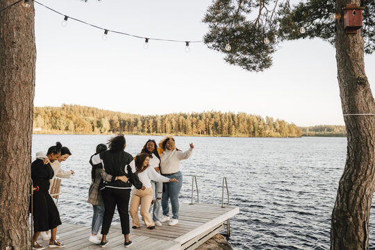 Young female friends dancing on jetty over lake