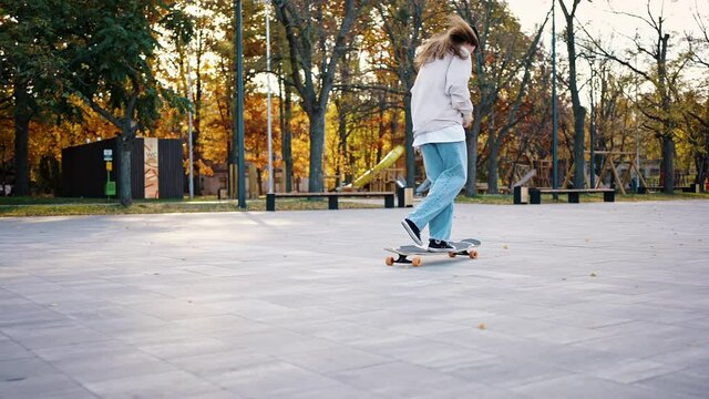 Young woman demonstrates jumps and tricks on a skateboard. Female skateboarder doing cross-step on her longboard while walking in the park