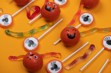 Halloween candy with black spiders,cobweb,smiling pumpkins  and tasty jelly worms on orange color...