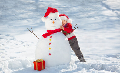 A child girl dressed in a Santa hat and a red sweater makes a big Snowman