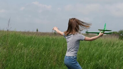 Preteen girl child playing with toy plane in the field with green grass. Pretty young female kid launching airplane at the nature. Concept of freedom