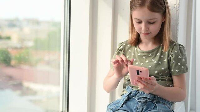 Preteen girl with smartphone sitting at home and looking social media, typing. Cute female kid with cell phone indoor