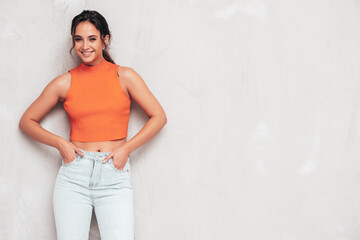 Young beautiful smiling female in trendy summer clothes. Sexy carefree woman posing near grey wall...
