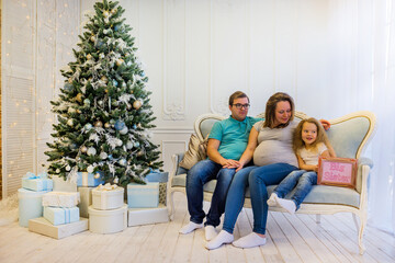 Family portrait near christmas tree. Pregnant woman