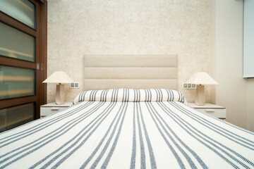 Modern bedroom interior design and beige wall texture background with a fabric headboard and striped sheets. Along with bedside tables and modern bedside lamps. High quality photo