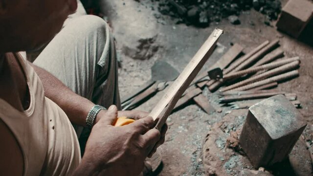 Blacksmith measuring a length of a tool, in smithy workshop