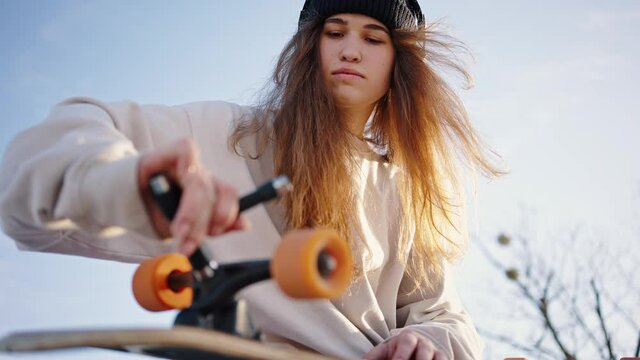Bottom view close up portrait of young beautiful female skater. A student repairs her skate using a T-key. Tighten the nuts on the longboard. Skate board tool, allen kay