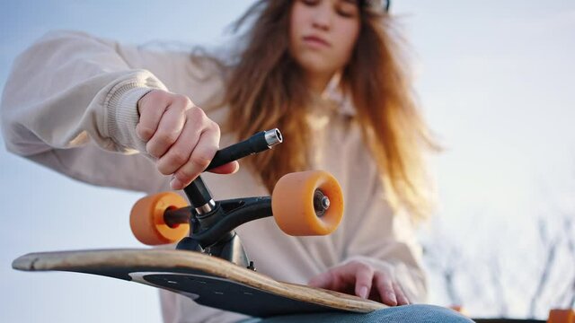 Student repairs her skate using a T-key. Tighten the nuts on the longboard. Skate board tool, allen kay. Bottom view close up portrait of young beautiful female skater