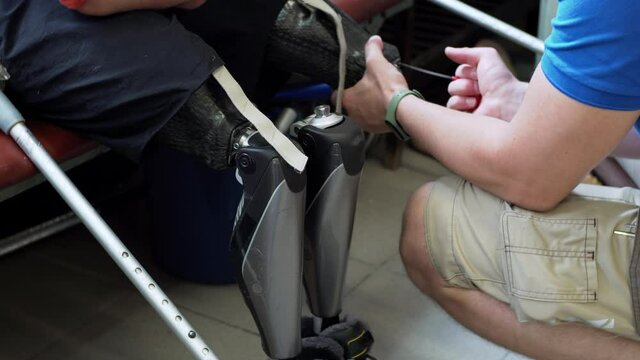 A medical engineer checks the artificial bionic leg prothesis device unscrewing its parts. Maintenance of a modern bionic legs prothesis for a man living with a disability with amputated legs