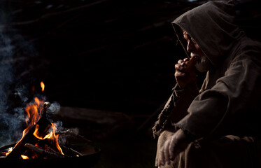 Old poor man sitting by the fire with a flute in the Middle Ages © Thomas Mucha