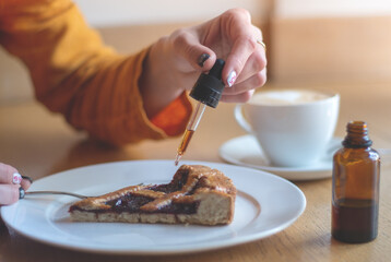 A girl in a yellow jacket is having breakfast in a cafe. Women's hands add THC and CBD oil to cherry pie. The concept of using medical marijuana.