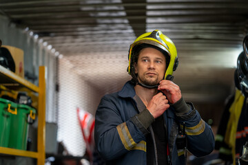 Portrait of fireman wearing firefighter turnouts while standing at fire station against uniforms...