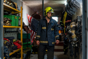Brave young fireman wearing protective uniform standing in fire department at fire station.