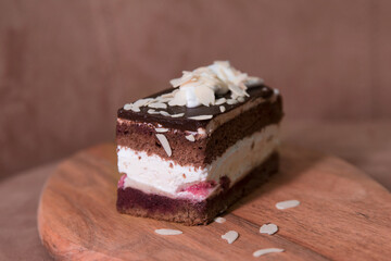 A piece of cherry cake, sprinkled with almonds, on a wooden board