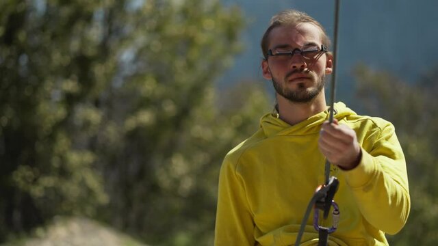 Young attractive man rock climber in the mountains belaying climbing partner and setting up rope, healthy lifestyle and fitness. man looking up through specialized climbing eyeglesses with prisma