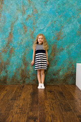 Cute girl in striped clothes standing near the wall