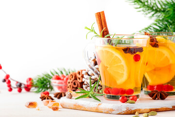 Fototapeta premium Winter hot tea with lemon, cranberries, herbs and spices in Christmas or New Year table setting, white background, copy space