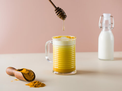  A drop of honey drips into a latte turmeric mug. Moon milk for better sleep. 