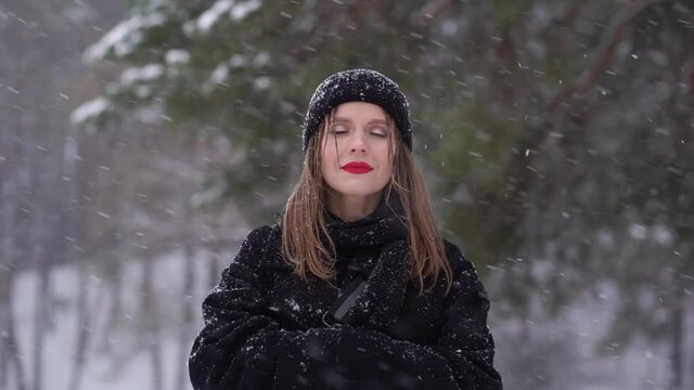 Video portrait of beautiful happy attractive european woman enjoying winter snowy weather outdoors in cold white frosty landscape. Video portrait of happy woman standing happily under falling snow