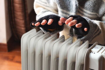 Person heating their hands at home over a domestic portable radiator in winter - obrazy, fototapety, plakaty