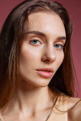 Close-up portrait of young beautiful girl without makeup isolated over dark pink studio background. Natural beauty concept.