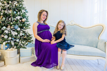 Beautiful pregnant woman in an ultraviolet dress sitting with daughter