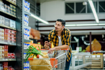 Young handsome man in a supermarket using smartphone while grocery shopping
