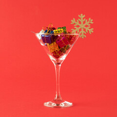 Christmas gifts in martini cocktail glass with snowflake on red background. Minimal New Year party concept.
