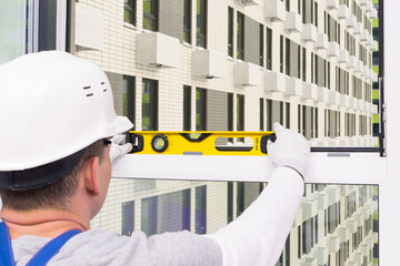 a man in a helmet checks the level of the windows after installing them