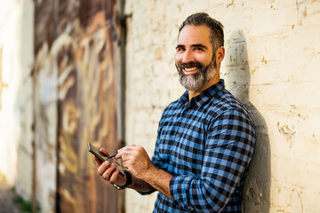 Businessman with a beard using mobile phone with digitized pen while standing in front of wall.