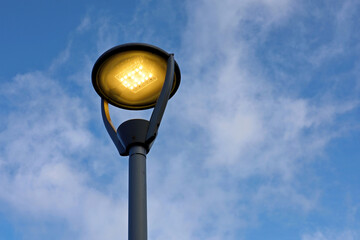 Glowing led lamp on background of blue sky with white clouds. Electric lighting, energy-saving...