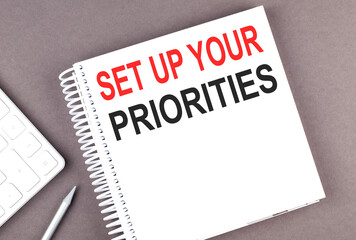 SET UP YOUR PRIORITIES text on the notebook with calculator and pen