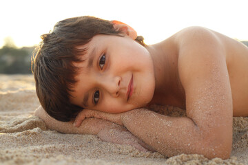 niño feliz tumbado en la playa con luz dorada del atardecer