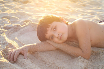 niño feliz tumbado en la playa con luz dorada del atardecer - 468158796