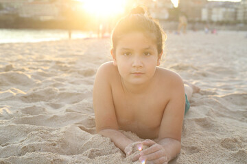 niño feliz tumbado en la playa con luz dorada del atardecer - 468158797