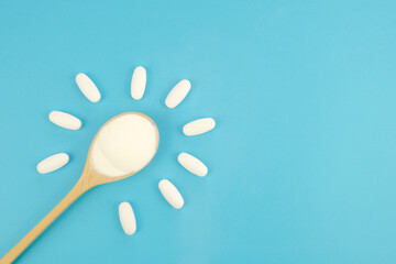 Hydrolyzed Marine Collagen Powder in wooden spoon and Vitamins in white tablets on blue background. Banner about health, taking vitamins. Creative background about drugs and food supplements. Top view