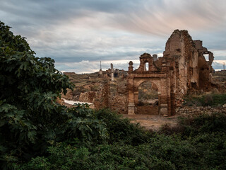 ruinas del pueblo viejo de Belchite con el cielo nublado y árboles en primer plano