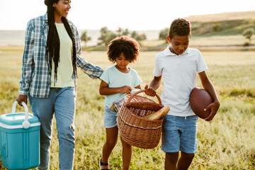 Black mother walking with her sons on summer field during picnic