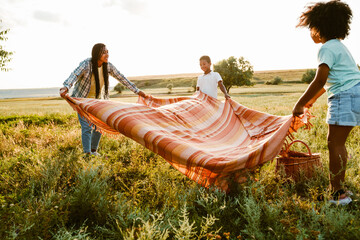 Black family laying blanket on summer field during picnic