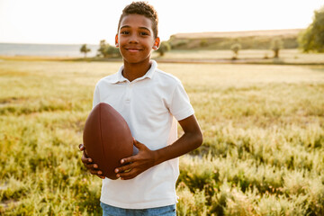 Black boy wearing white shirt smiling while posing with rugby ball