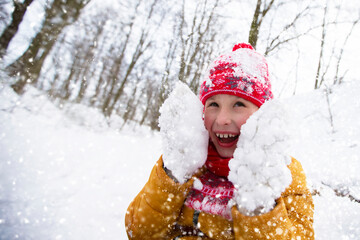 Little boy in bright winter clothes and fur mittens in the snow. Child on a cold winter day.