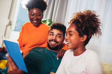 Happy african american family reading book together, staying at home during coronavirus quarantine