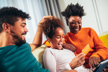 Online Shopping. Happy african family having fun using credit card and digital tablet at home.