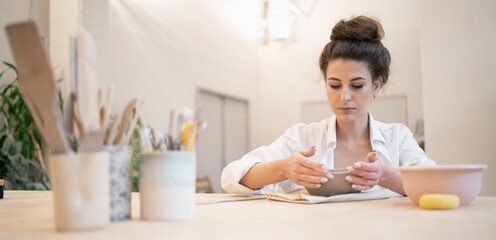 Master in the ceramics studio. A uniform of convenient and comfortable work. Clay and porcelain dishes to order. Ceramist woman in the workshop. Individual products for the home.