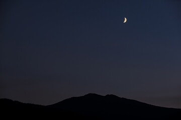 Bright crescent in dark sky over mountains